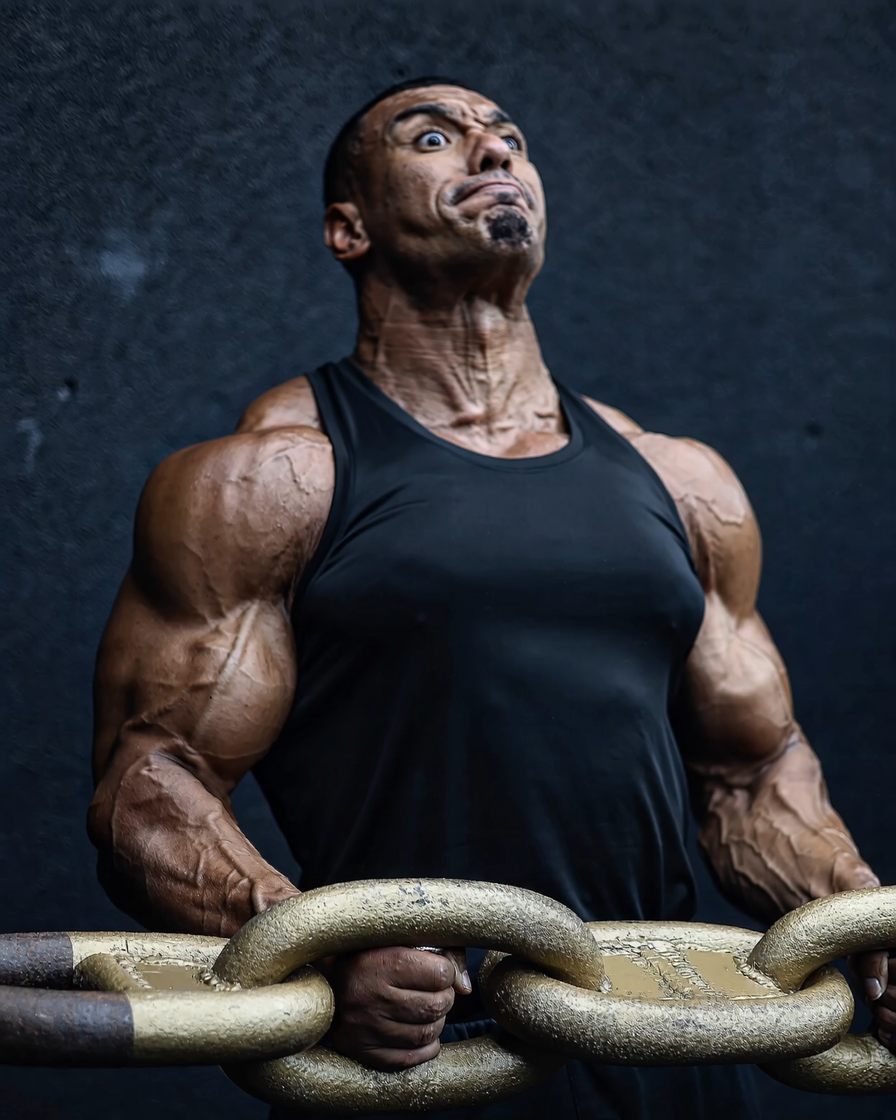 Larry Wheels in a black tank top holding a heavy steel chain in a dark studio